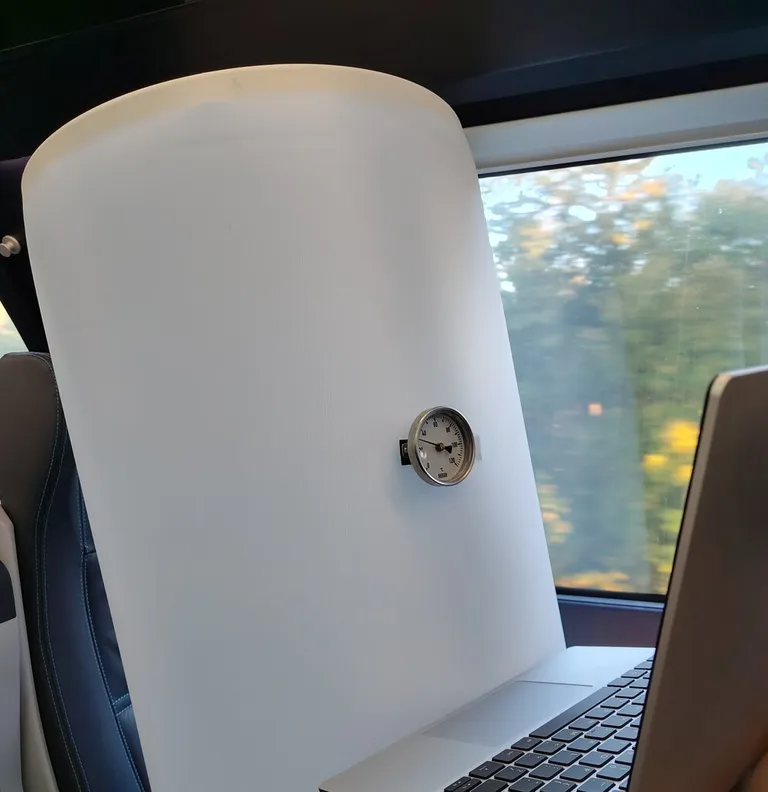 Bert der Boiler, ein weißer Warmwasserboiler, sitzt mit einem Laptop im Zug